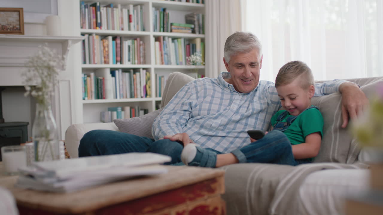 happy grandfather showing little boy how to use smartphone teaching curious grandson modern technology intelligent child learning mobile phone sitting with grandpa on sofa