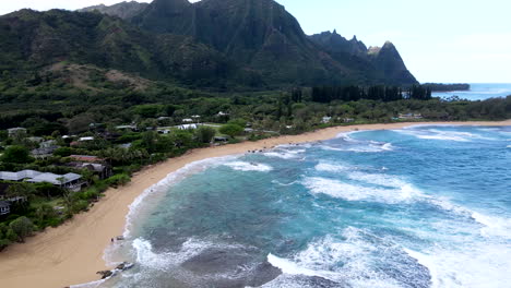 aerial zoom toward haena on clear day as waves roll in