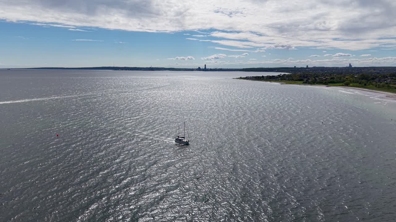 Aerial drone video of a small boat cruising across rippling water under a partly cloudy sky near the shoreline