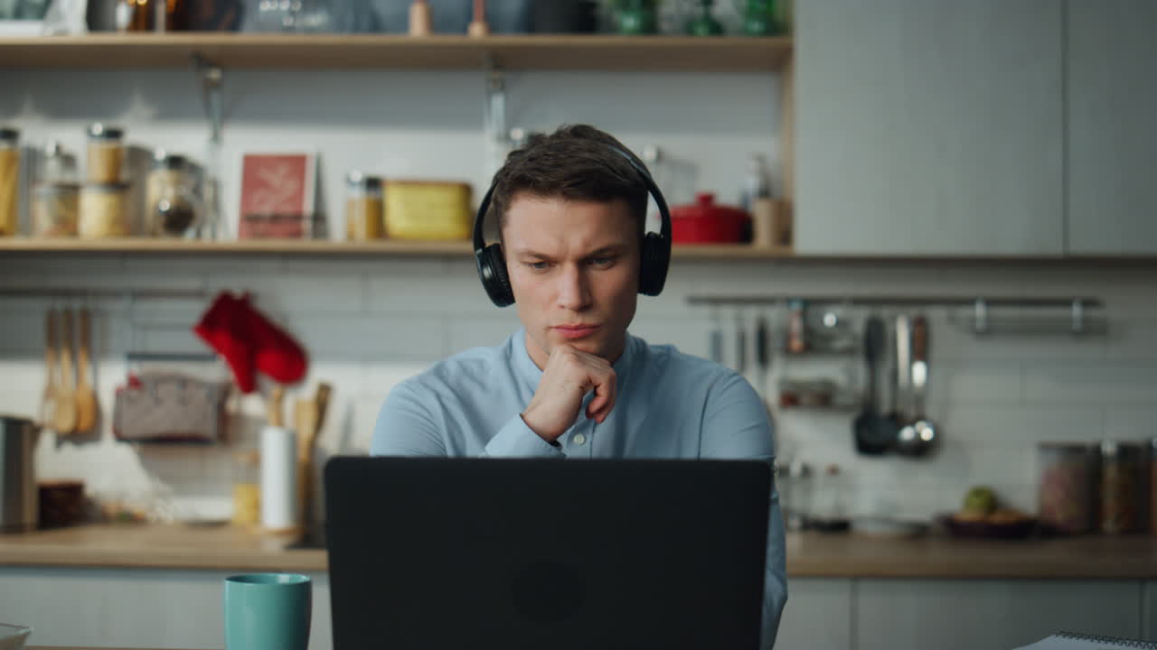 Man listening educational seminar in kitchen with headphones. Student studying.
