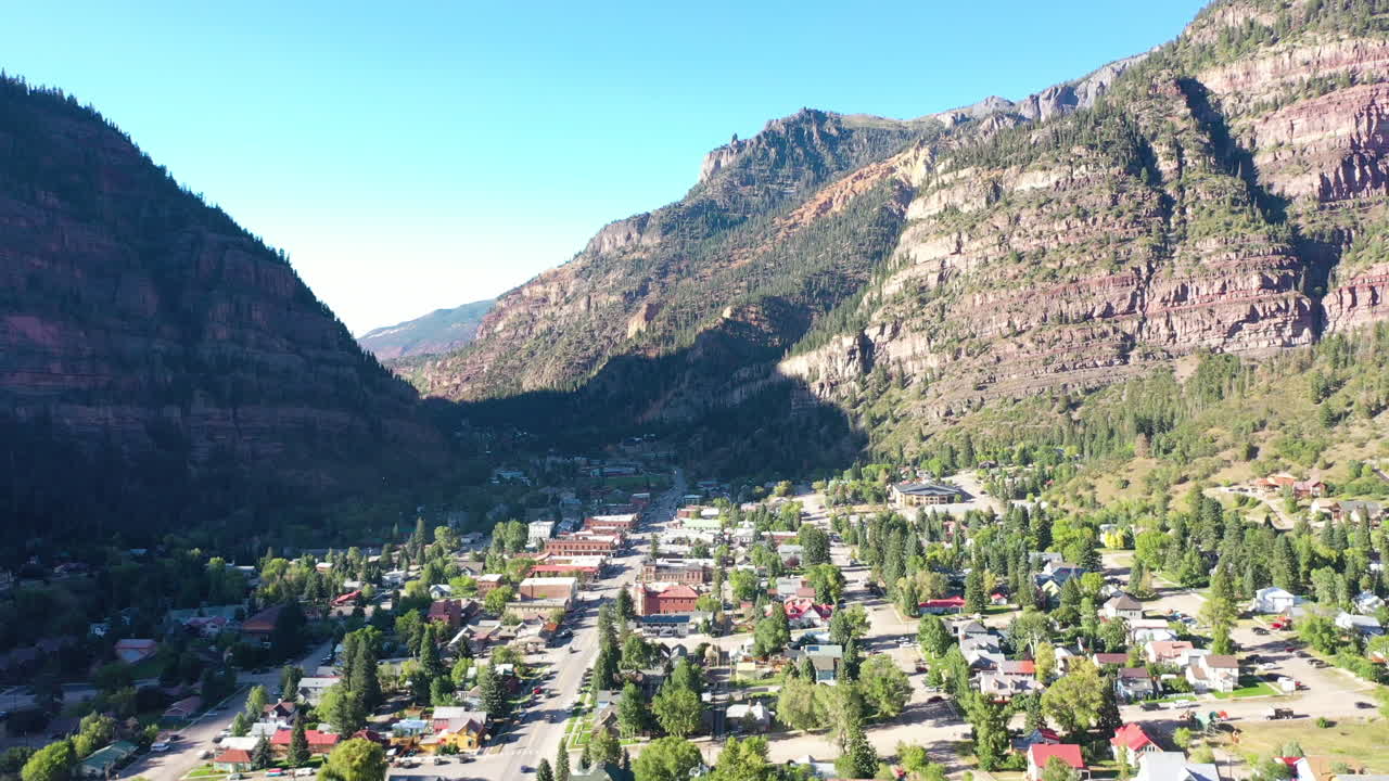 drone aéreo bajando el movimiento de la ciudad montañosa de ouray colorado, automóviles conduciendo a través de la ciudad y casas rodeadas de acantilados rocosos de montaña y pinos para