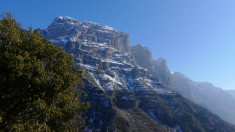 Rocky-and-snowy-mountain-tops-appear-behind-tree-in-Zagori,-Greece