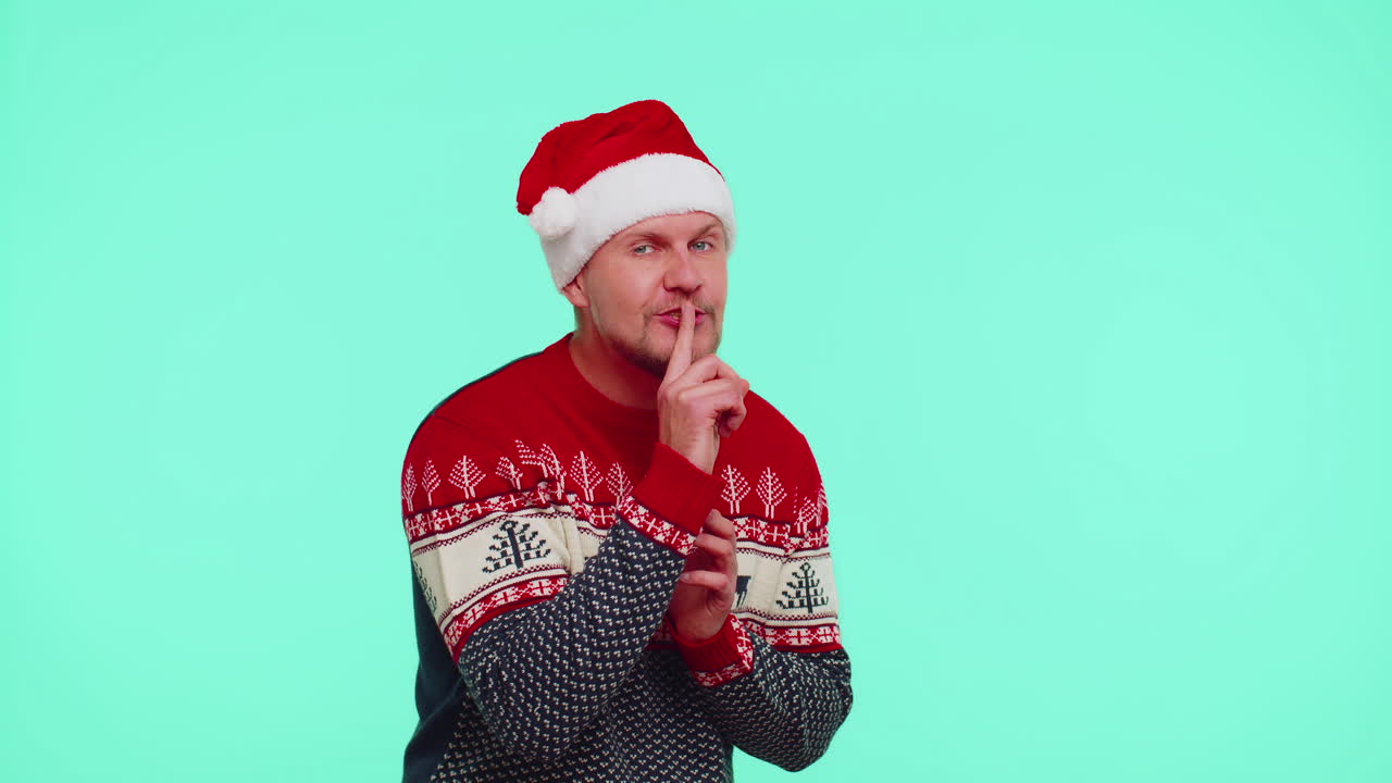 赤いクリスマスセーターを着た男性指差し指を唇に押し静けさを示すジェスチャーシグナル秘密