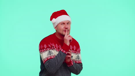Man-wears-red-Christmas-sweater-presses-index-finger-to-lips-makes-silence-gesture-sign,-secret