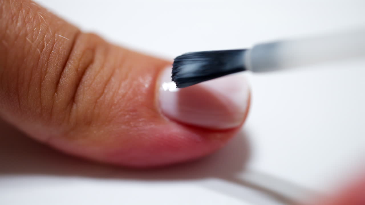 Close up of a woman painting her nails with milky white nail polish