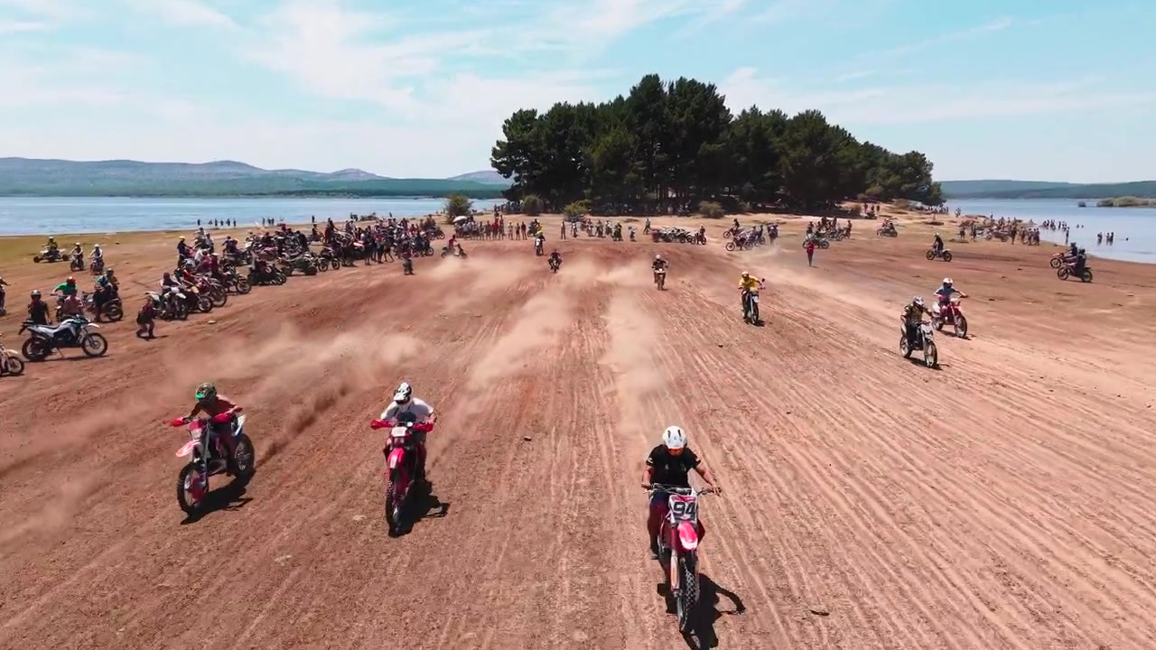 Pilotos de motocross correndo em pista de terra perto do lago