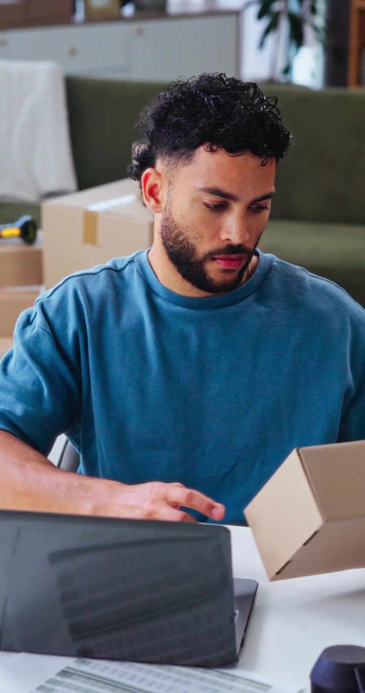 Young Man Working on Laptop and Packing Cardboard Box in Office