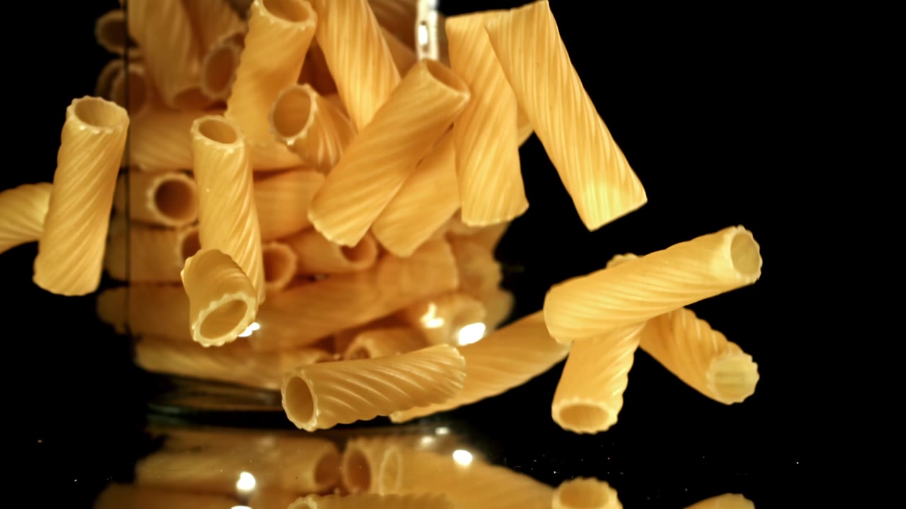 Rigatoni secchi che cadono al rallentatore su sfondo nero