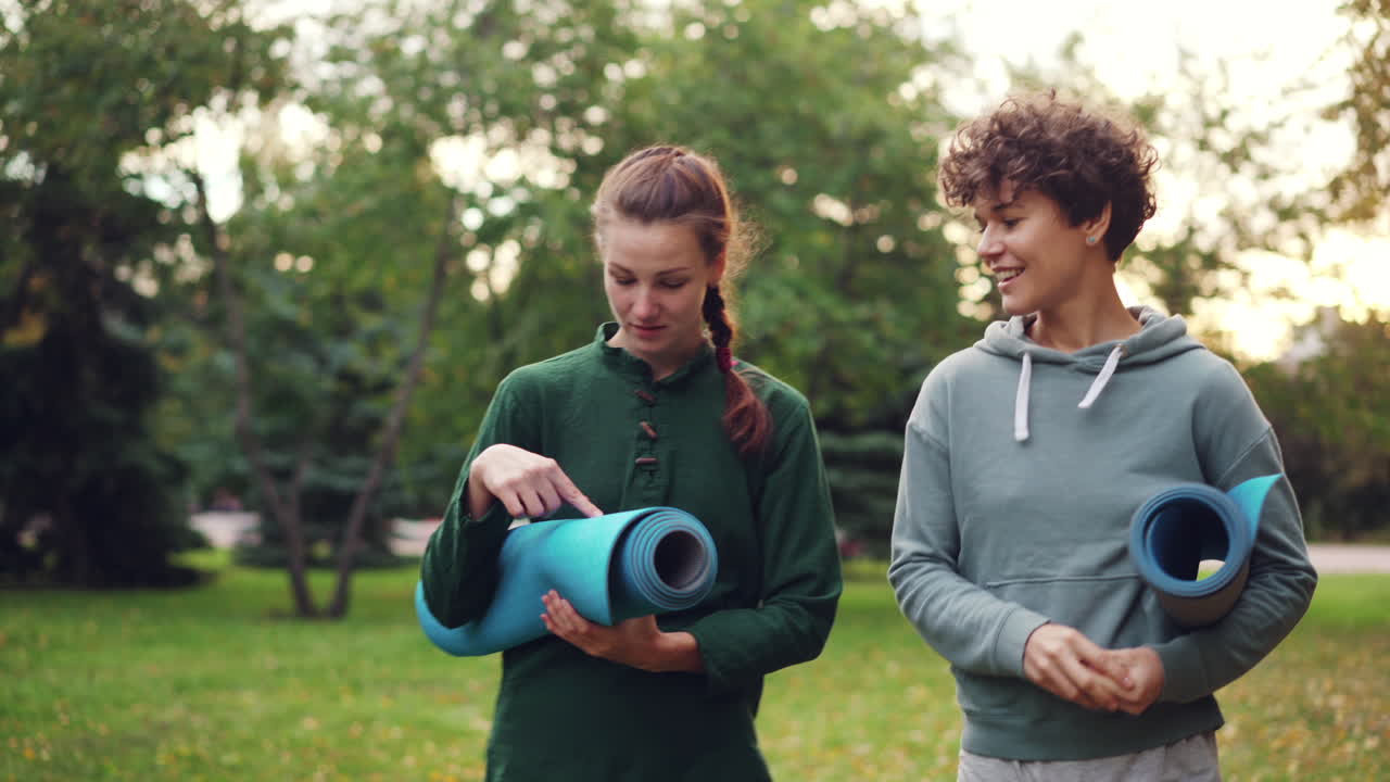 Two women walking in a park with yoga mats