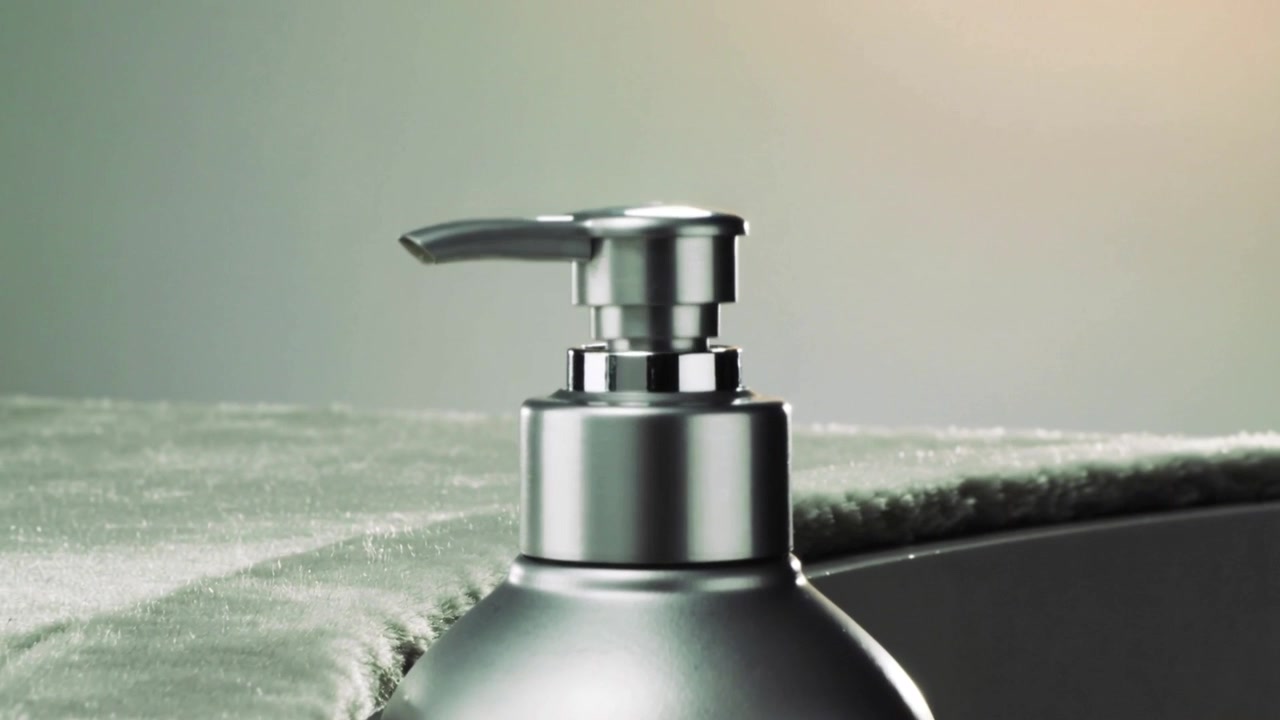 Zooming camera revealing silver pump dispenser at vanity, showcasing chrome nozzle, towel, rim