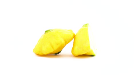 one whole and one half of yellow patisson squashes with water drops. rotating on the turntable. isolated on the white background. close-up. macro.