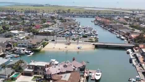 aerial wide view of luxury bayfront homes glides in closer to reveal a private beach and docked luxury boats