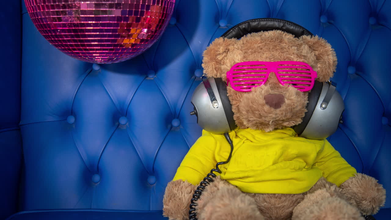 oso de peluche con auriculares y pelota de discoteca en un sofá azul