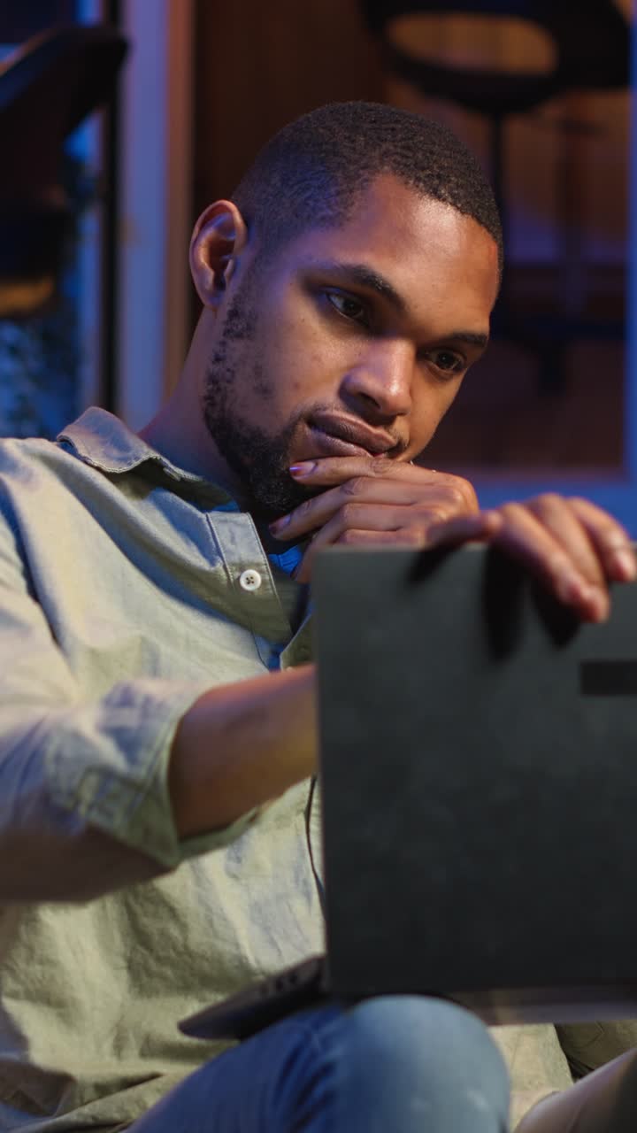 Vertical Video Black man taking a break from work by scrolling his smartphone at home