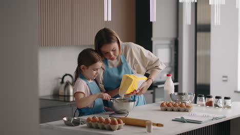 little girl and her mother are cooking dough for cake in home kitchen mom and daughter are spending time together