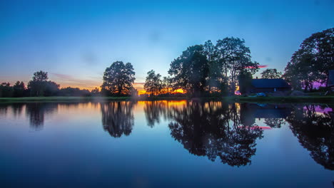 Zeitrafferaufnahme-Eines-Wunderschönen-Goldenen-Sonnenuntergangs-Hinter-Einem-Ruhigen-See-In-Der-Wildnis-Am-Abend---Spiegelung-Der-Baumsilhouette-Auf-Der-Wasseroberfläche