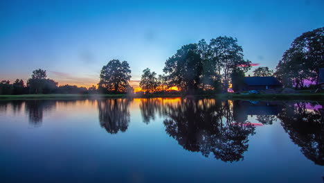 tiro de lapso de tiempo de la hermosa puesta de sol dorada detrás de un lago tranquilo en el desierto por la noche - reflejo de la silueta del árbol en la superficie del agua