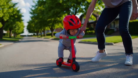 mother helping child learn to ride a scooter in a sunny neighborhood