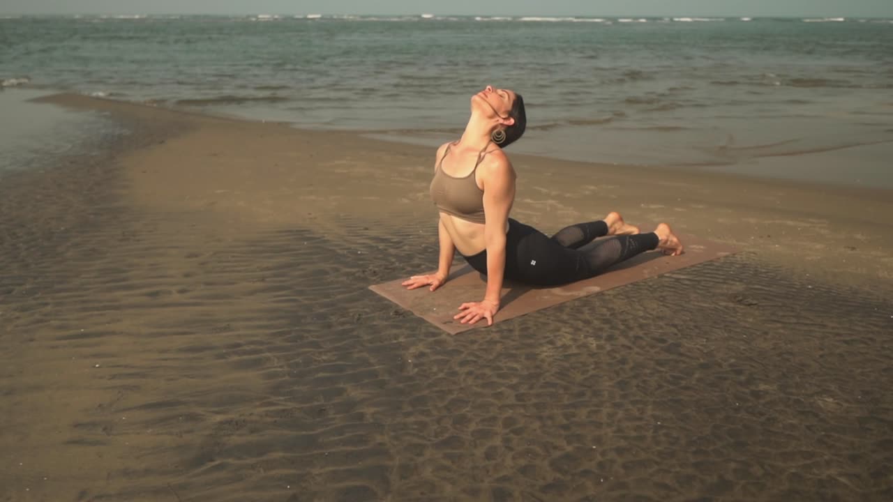 insegnante di yoga che fa piegare il cane rivolto verso l'alto mentre insegna a una lezione sulla spiaggia