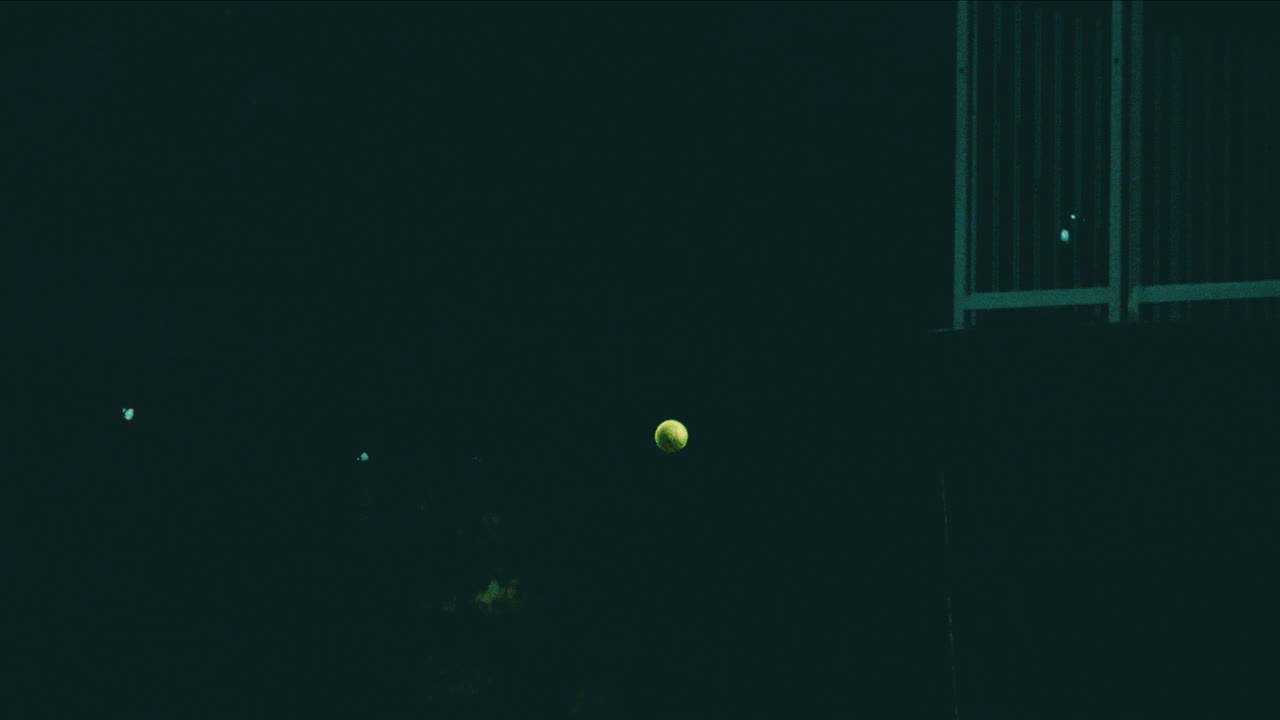 테니스 공이 야간에 극도로 느린 동작으로 떠다니며 경기장 조명에 의해 조명됩니다, 4k 800fps 테니스 공은 공중에 얼어붙습니다.