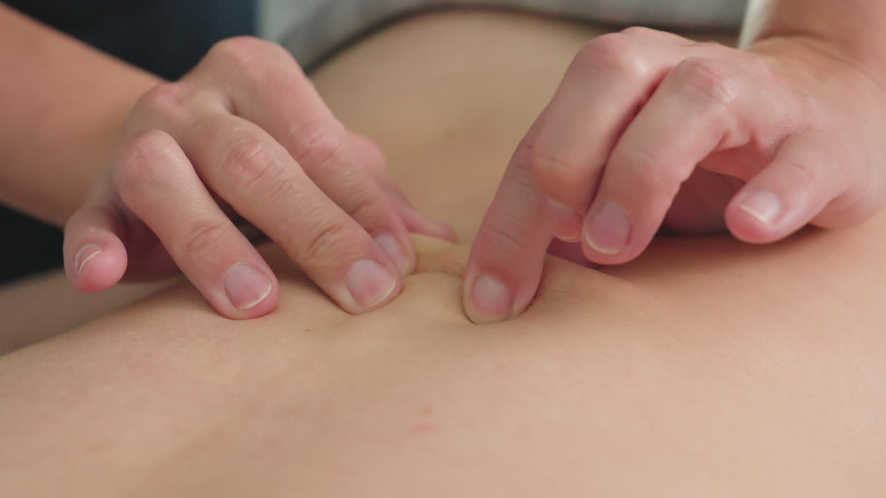 Close up of woman back being massaged by beautician fingertips moving in circular kneading motions on massage bed under soft ambient lighting in spa room conveying soothing relaxation