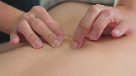 close up of woman back being massaged by beautician fingertips moving in circular kneading motions on massage bed under soft ambient lighting in spa room conveying soothing relaxation