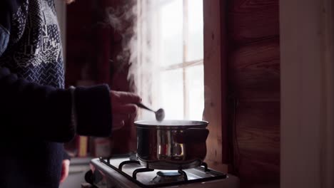 a man stirs the contents of a casserole as he cooks in bessaker, trondelag county, norway - close up