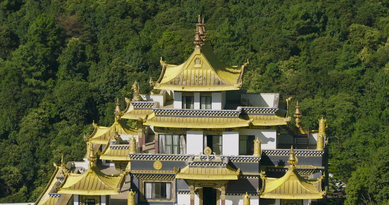 Drone kredser langsomt om det øverste gyldne tag på den buddhistiske klosterbygning i Pharping, Nepal, og viser den grønne bjergskråning i baggrunden på en lys solskinsdag