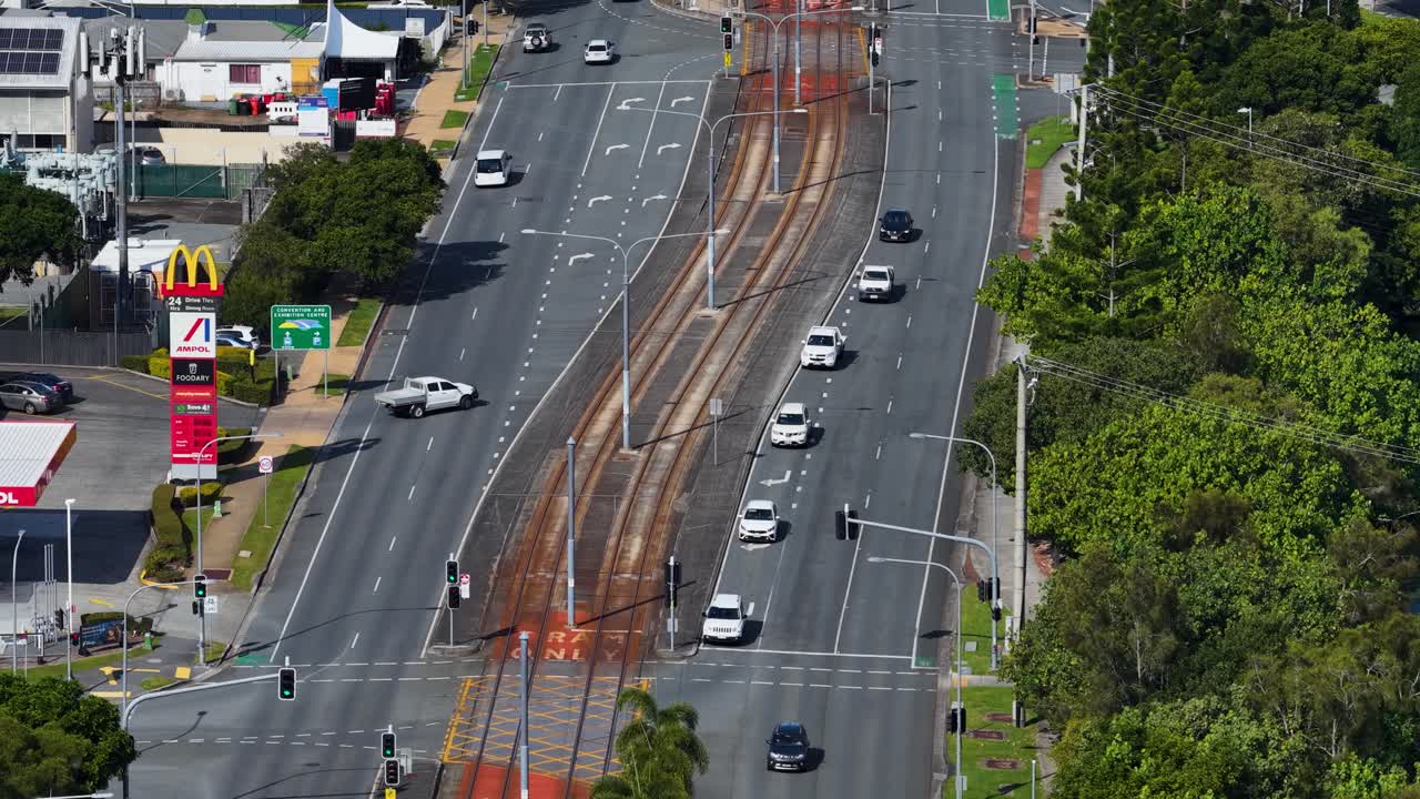 Aerial footage shows light rail tracks and vehicles on a busy highway in Broadbeach, Queensland, under clear daylight