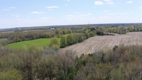 A-fast-shot-flying-over-the-forest-then-showcasing-farmers-fields-located-in-Puslinch,-Ontario