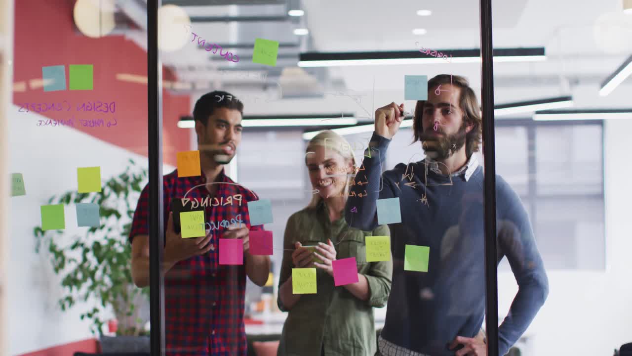 Diverse office colleagues writing on glass board and discussing together at modern office