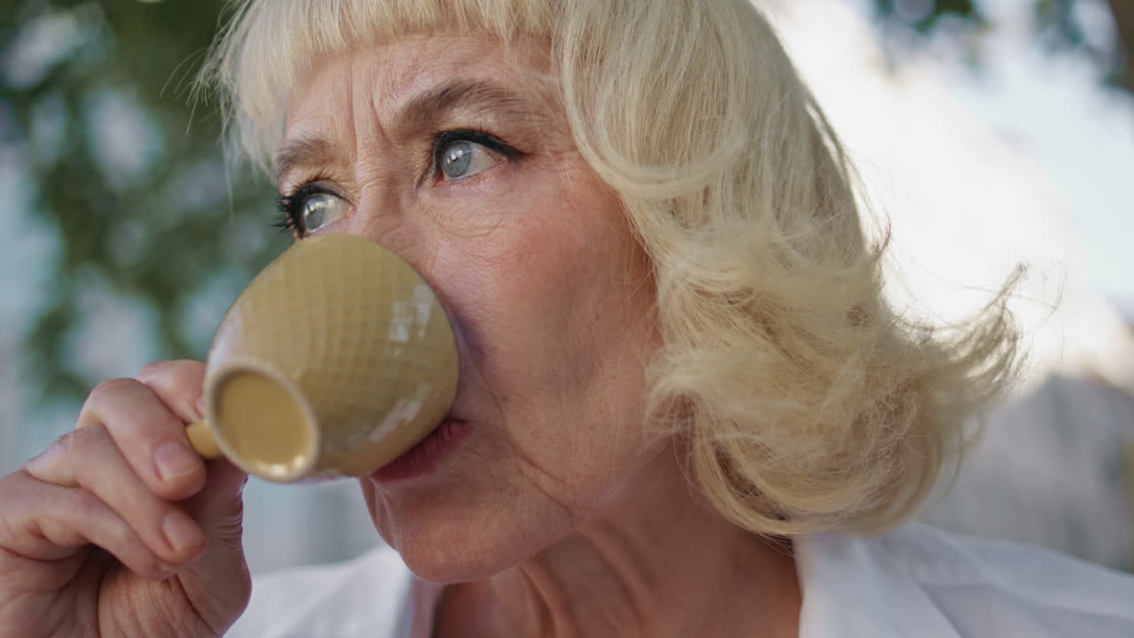 Primo piano di una donna matura che si gode un caffè per strada. Ritratto di un'anziana signora che beve.