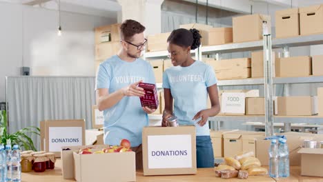 hombre caucásico y joven voluntaria afroamericana empacando cajas de donación con comida en un almacén de caridad