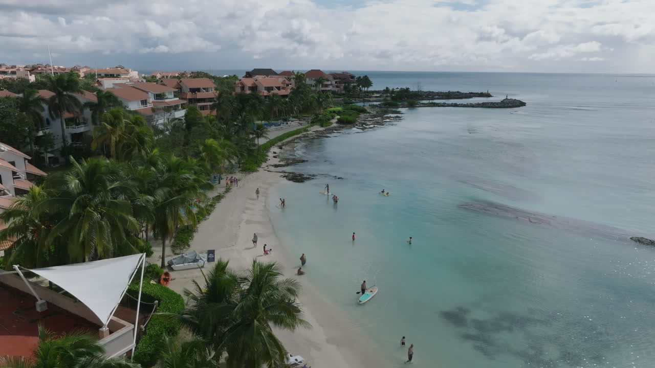 impresionante toma aérea de dolly que se mueve desde la costa residencial de vacaciones, revelando una hermosa playa y un mar y cielo tranquilos con nubes en un día soleado en el caribe