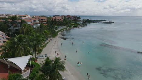 Stunning-Aerial-Dolly-Shot-Moving-in-from-Holiday-Residential-Seashore,-Revealing-a-Beautiful-Beach-and-Calm-Sea-and-Sky-with-clouds-on-a-sunny-day-in-Caribbean