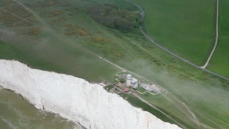 Flying-around-Belle-Tout-Lighthouse,-white-cliffs,-foggy-sky-and-sea