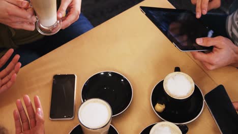 friends using mobile phone and digital tablet while having cup of coffee