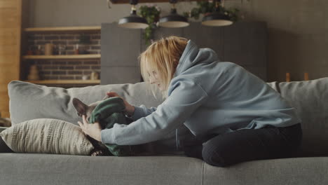 Rothaarige-Frau-Kleidet-Ihre-Bulldogge-Mit-Einem-Pullover,-Während-Sie-Zu-Hause-Auf-Dem-Sofa-Im-Wohnzimmer-Sitzt