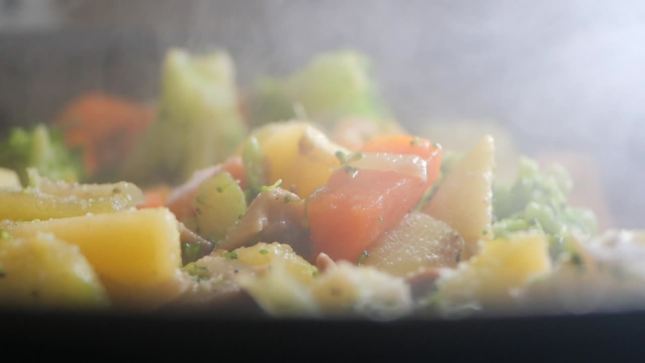 Primer plano de verduras mixtas humeantes siendo sazonadas