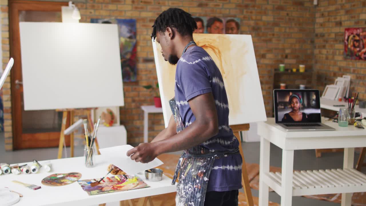 pintor afroamericano que sostiene una fotografía y mezcla pintura en el estudio del artista