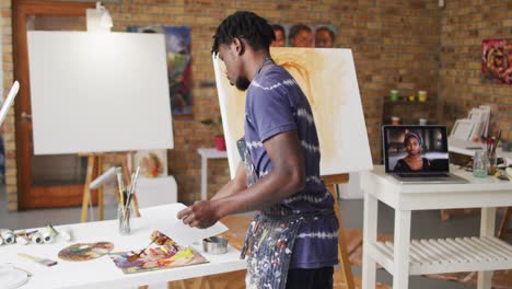 African-american-male-painter-holding-photograph-and-mixing-paint-in-artist-studio