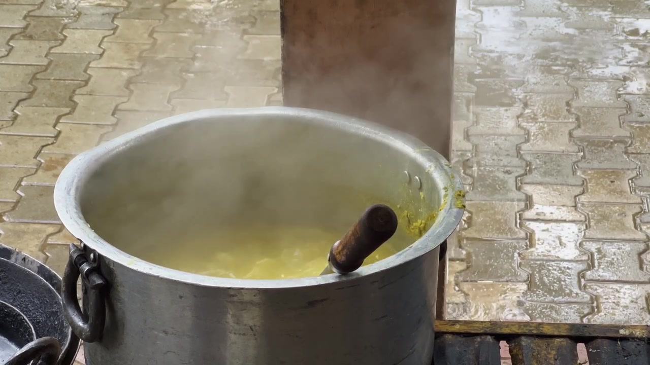 Cucina all'aperto in stile Dhaba con una grande pentola di metallo durante il tempo piovoso, che mostra la preparazione tradizionale del cibo accanto a una tavola calda lungo la strada