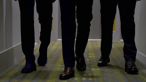 close-ups of the legs and shoes of three men walking down a hotel corridor, they are dressed in suits