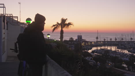 man captures sunset sky at harbor bay, with port sailboats and palms