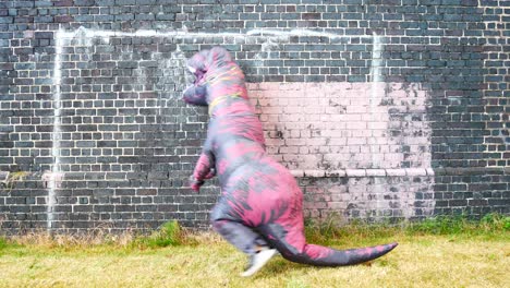 divertido disfraz de dinosaurio prehistórico saltando y bailando contra la pared de ladrillo