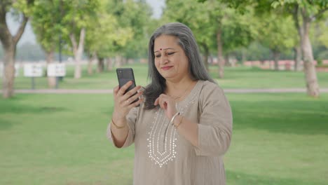 Glückliche-Alte-Indische-Frau-Blättert-Durch-Telefon-Im-Park