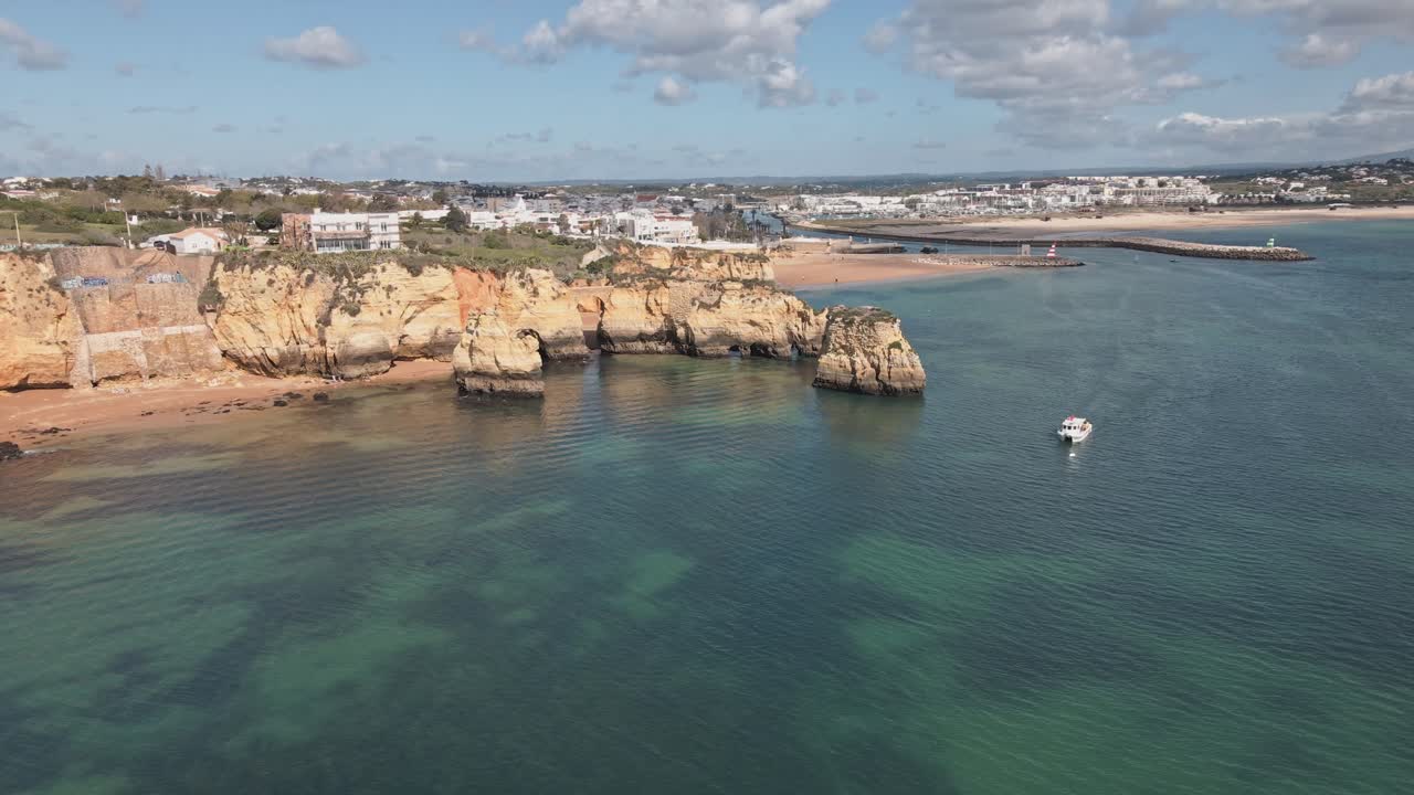 Un dron aéreo realiza una órbita helicoidal alrededor de unos acantilados dorados, escarpadas formaciones rocosas y aguas turquesas, revelando las playas vírgenes y la costa cerca de Lagos, Portugal