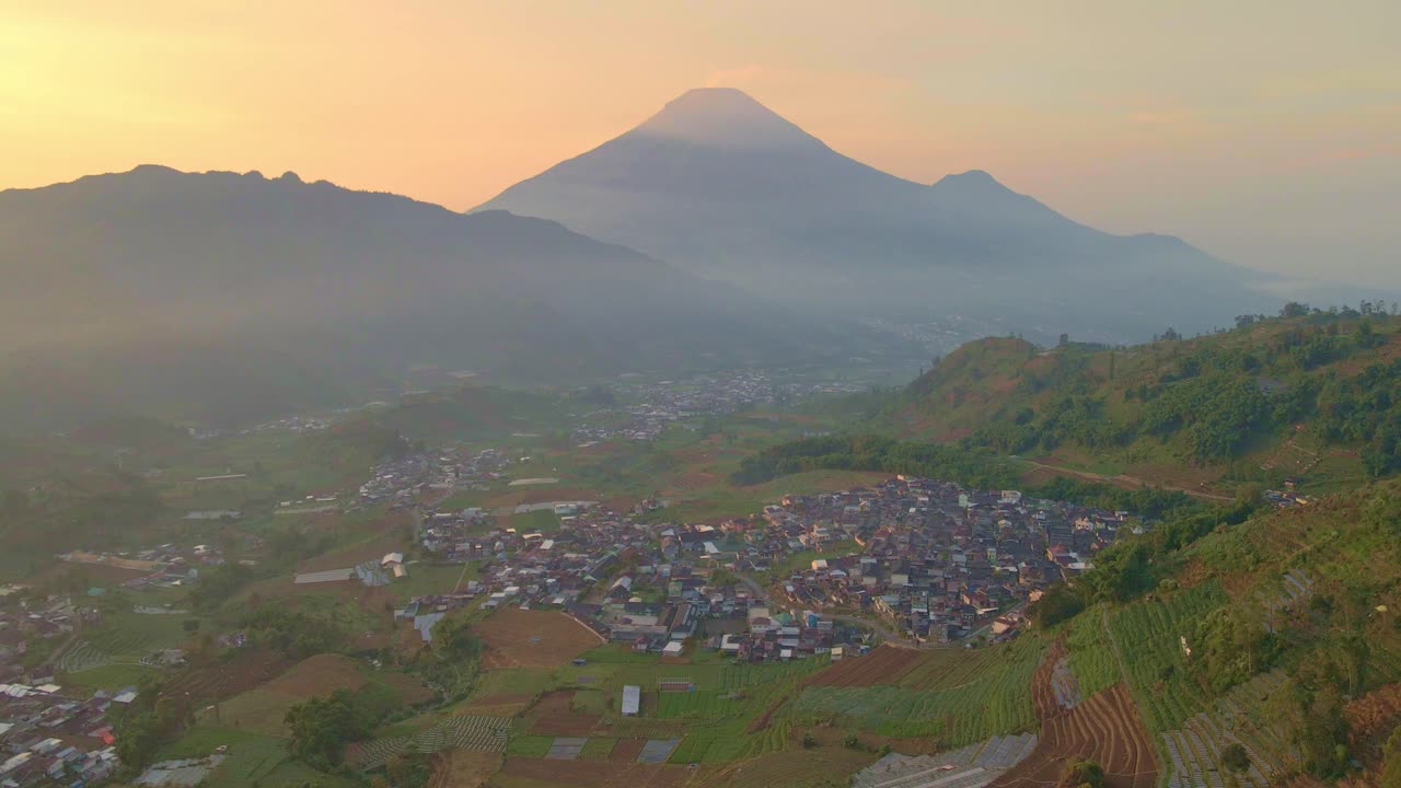 Pemandangan udara desa di lembah di antara pegunungan dengan langit matahari terbit yang indah dan latar belakang pegunungan