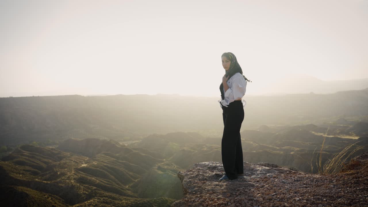 Young woman wearing a hijab standing on a cliff edge at sunrise