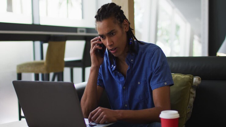 Mixed race man going through paperwork talking on smartphone using laptop in the office